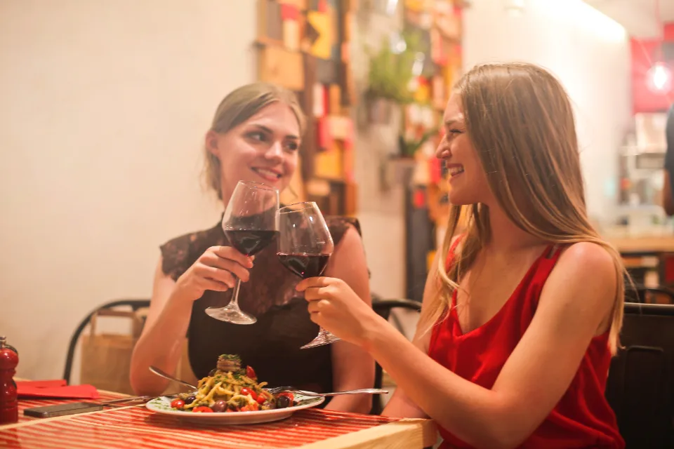 Two friends toasting glasses of red wine over dinner at a cozy restaurant table